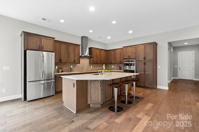 253 Stone Mountain Way, Denver, NC 28037 - kitchen featuring stainless steel appliances, wall chimney exhaust hood, a kitchen island with sink, decorative backsplash, and light countertops