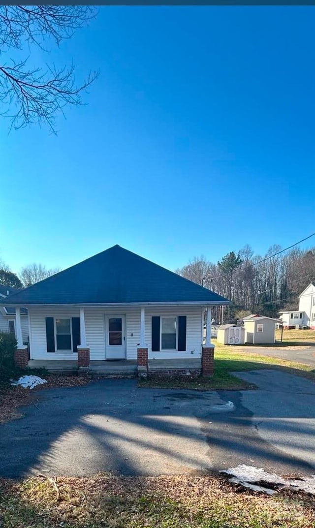 single story home featuring a porch and a storage shed