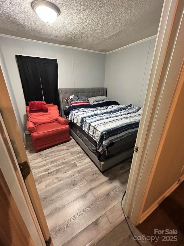 bedroom featuring a textured ceiling, hardwood / wood-style flooring, and ornamental molding