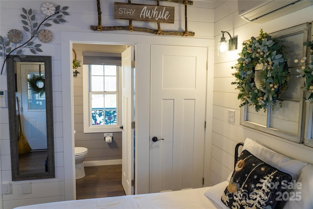 interior space featuring ensuite bath, wood-type flooring, wood walls, and a wall mounted air conditioner