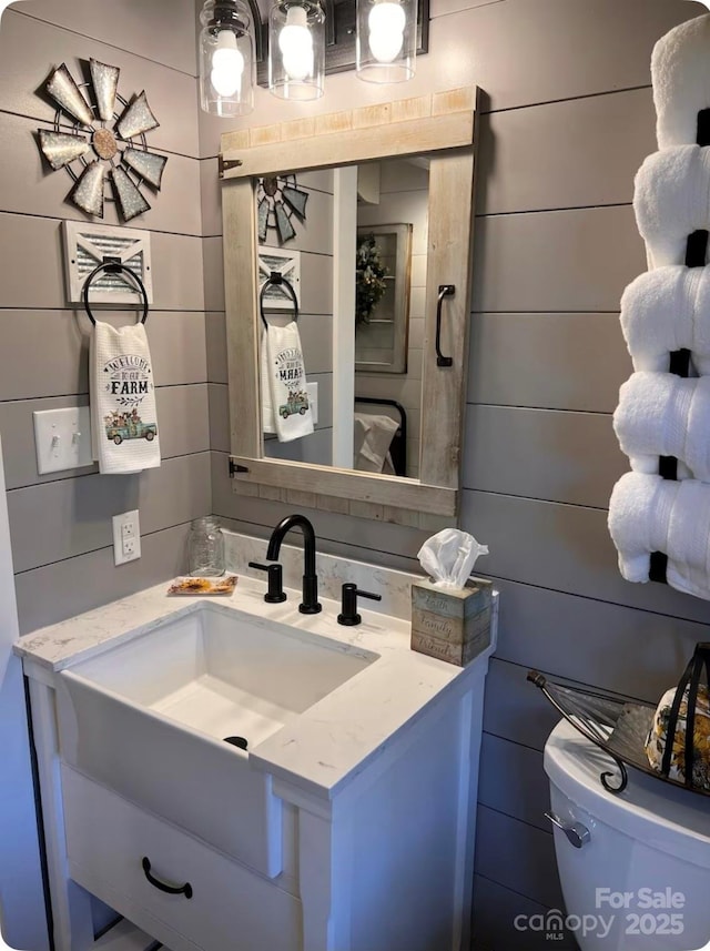 bathroom featuring toilet, vanity, and wooden walls