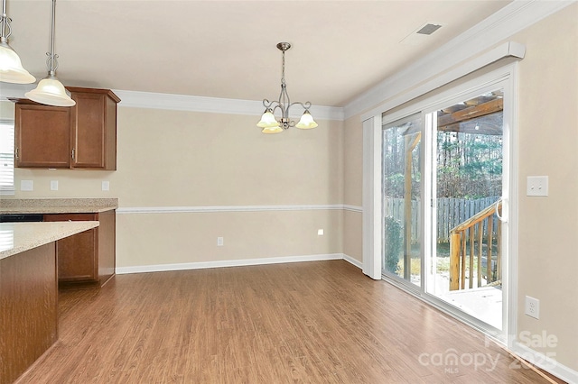 unfurnished dining area featuring a chandelier, wood-type flooring, plenty of natural light, and crown molding