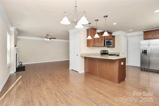 kitchen featuring kitchen peninsula, appliances with stainless steel finishes, ceiling fan with notable chandelier, crown molding, and decorative light fixtures