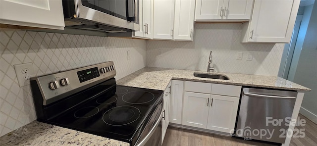 kitchen with light stone counters, stainless steel appliances, white cabinetry, and sink