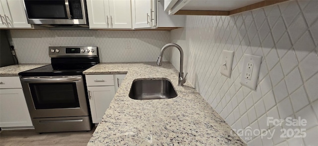 kitchen featuring backsplash, sink, light stone countertops, white cabinetry, and stainless steel appliances