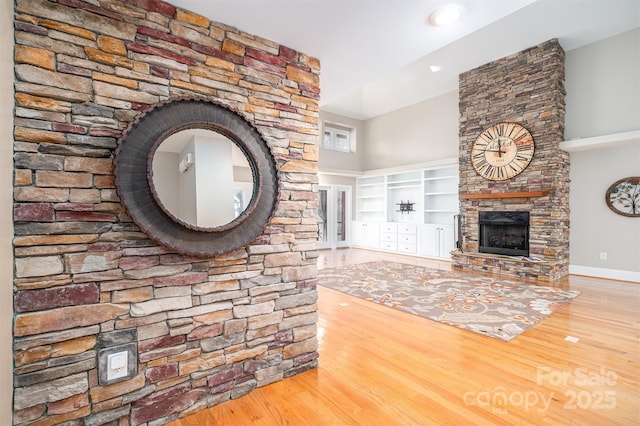 unfurnished living room featuring hardwood / wood-style floors, a stone fireplace, and built in shelves