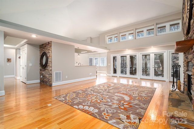 living room with a stone fireplace, french doors, high vaulted ceiling, and light wood-type flooring