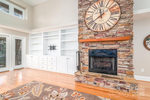 living room featuring a fireplace, a towering ceiling, light wood-type flooring, and a healthy amount of sunlight