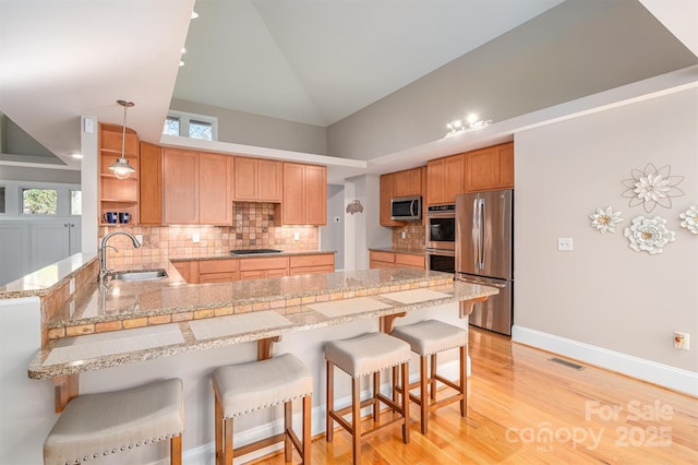 kitchen featuring sink, stainless steel appliances, backsplash, kitchen peninsula, and a kitchen bar