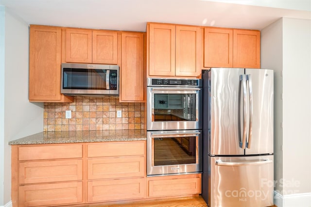 kitchen with light stone countertops, decorative backsplash, light brown cabinets, and stainless steel appliances