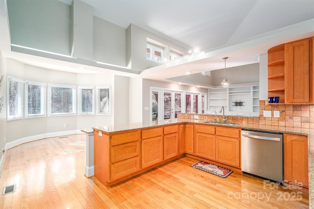 kitchen with kitchen peninsula, stainless steel dishwasher, sink, pendant lighting, and stone countertops