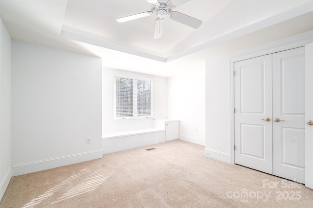 unfurnished bedroom featuring ceiling fan, light carpet, a tray ceiling, and a closet