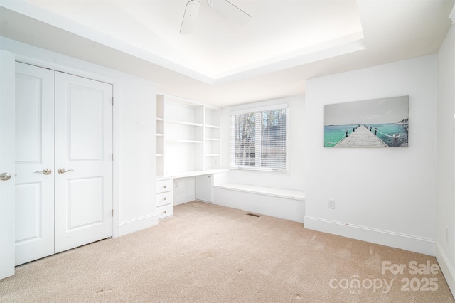 unfurnished bedroom featuring a tray ceiling, ceiling fan, a closet, and light colored carpet