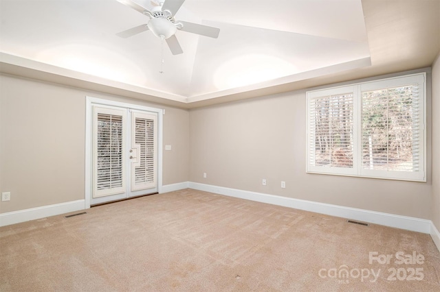 empty room with light carpet, french doors, a tray ceiling, and ceiling fan