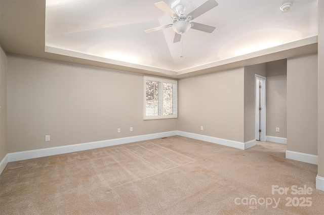 carpeted spare room with a raised ceiling and ceiling fan