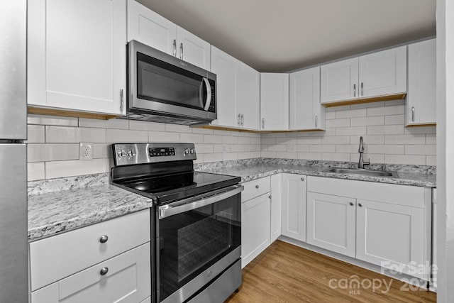 kitchen featuring sink, white cabinets, light hardwood / wood-style floors, decorative backsplash, and appliances with stainless steel finishes