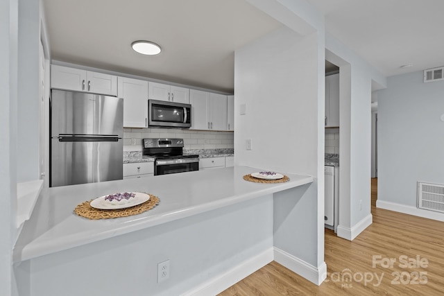 kitchen with stainless steel appliances, white cabinets, light hardwood / wood-style floors, tasteful backsplash, and kitchen peninsula