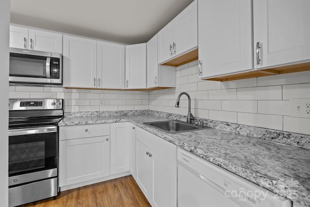 kitchen featuring light hardwood / wood-style floors, stainless steel appliances, decorative backsplash, sink, and white cabinetry