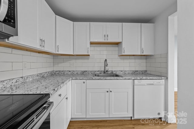 kitchen featuring white dishwasher, white cabinets, light stone countertops, and sink