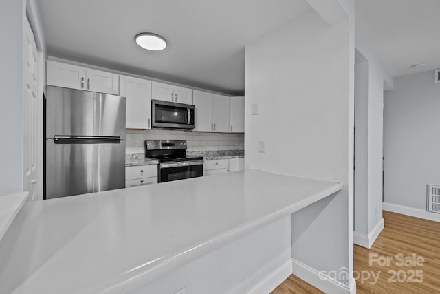 kitchen featuring appliances with stainless steel finishes, light hardwood / wood-style flooring, white cabinets, and decorative backsplash