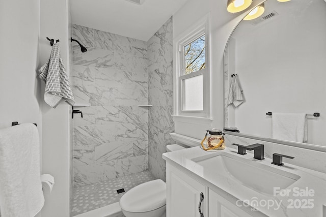 bathroom featuring a tile shower, vanity, and toilet