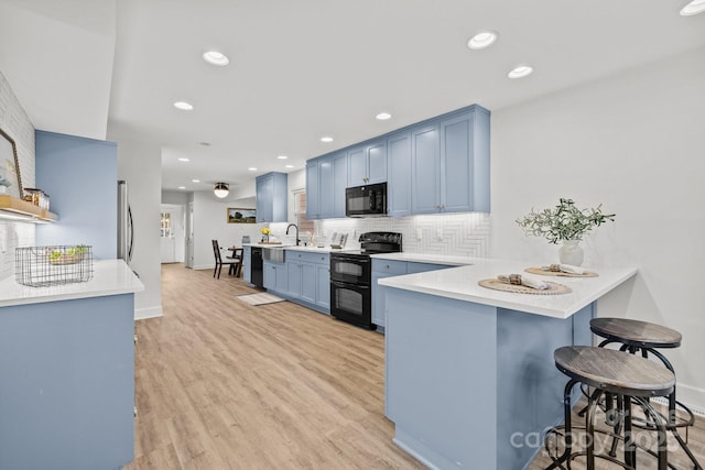 kitchen with blue cabinets, kitchen peninsula, a kitchen bar, decorative backsplash, and black appliances