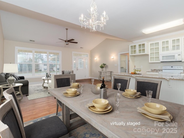 dining space featuring ceiling fan with notable chandelier, wood-type flooring, and vaulted ceiling