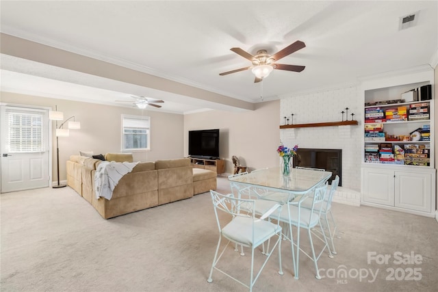 dining area with ceiling fan, crown molding, light carpet, and a brick fireplace