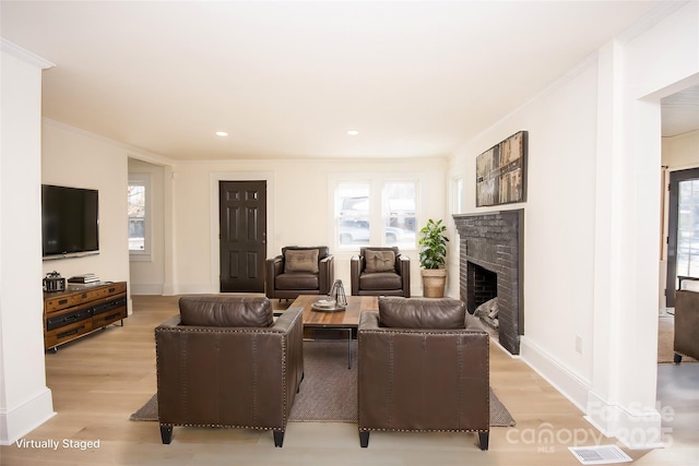 living room featuring a brick fireplace, ornamental molding, a healthy amount of sunlight, and light hardwood / wood-style flooring