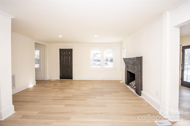 unfurnished living room featuring a brick fireplace, light hardwood / wood-style flooring, ornamental molding, and a healthy amount of sunlight