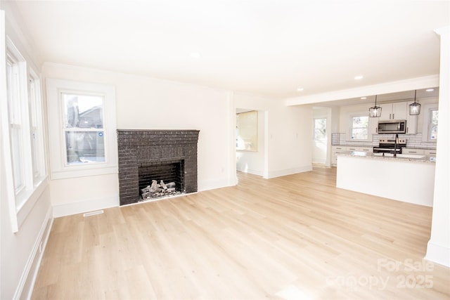 unfurnished living room featuring a brick fireplace and light hardwood / wood-style floors