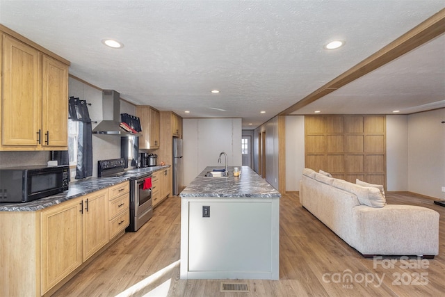 kitchen featuring a textured ceiling, appliances with stainless steel finishes, wall chimney range hood, light hardwood / wood-style floors, and a center island with sink