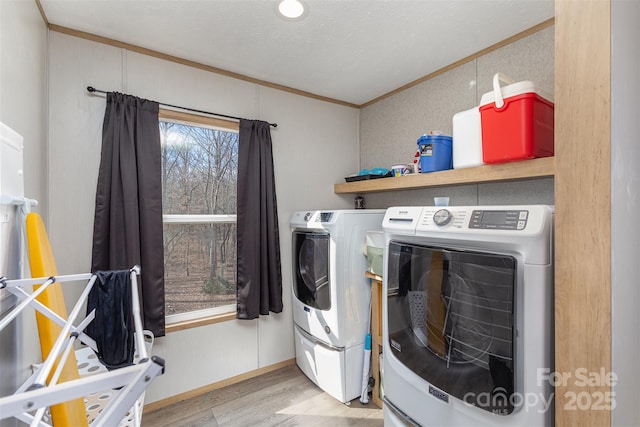 clothes washing area with light hardwood / wood-style floors, a textured ceiling, ornamental molding, and washing machine and dryer