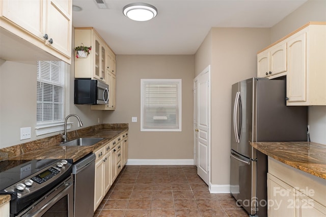 kitchen featuring sink, stainless steel appliances, tile patterned floors, dark stone countertops, and cream cabinetry