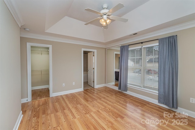 unfurnished bedroom with a raised ceiling, ceiling fan, crown molding, a spacious closet, and light hardwood / wood-style flooring