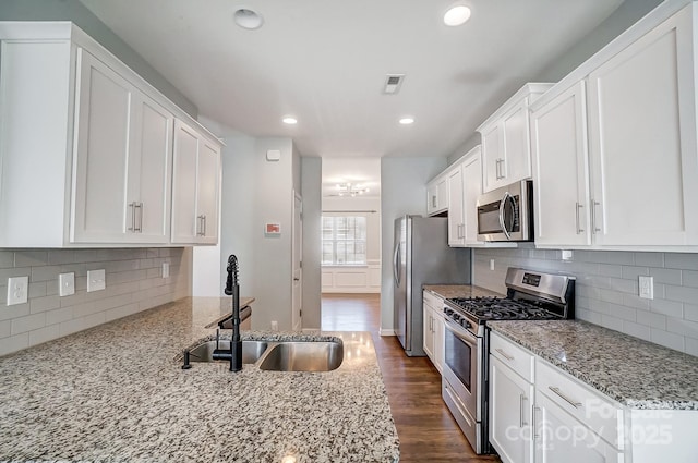 kitchen with sink, stainless steel appliances, light stone counters, backsplash, and white cabinets