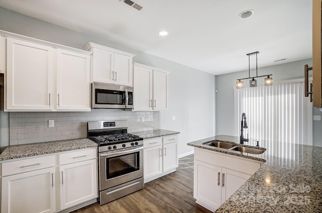 kitchen with light stone counters, stainless steel appliances, white cabinetry, and sink