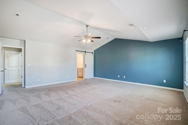 unfurnished room featuring ceiling fan, a barn door, light colored carpet, and vaulted ceiling