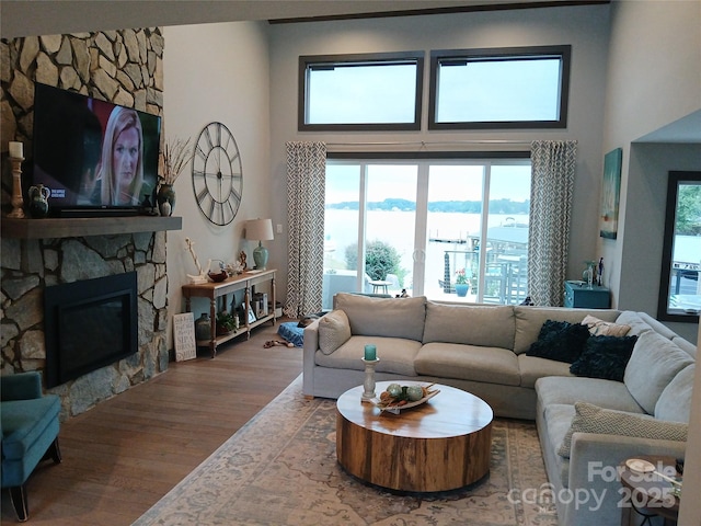 living room featuring wood-type flooring, a stone fireplace, and a high ceiling