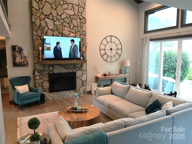 living room with a stone fireplace, a towering ceiling, and hardwood / wood-style flooring