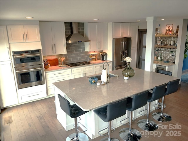 kitchen with white cabinetry, stainless steel appliances, and wall chimney range hood