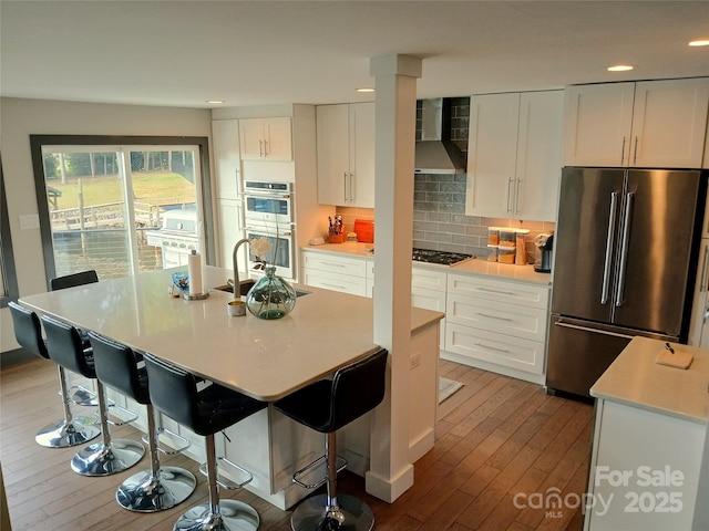 kitchen with white cabinetry, appliances with stainless steel finishes, a center island with sink, and wall chimney exhaust hood