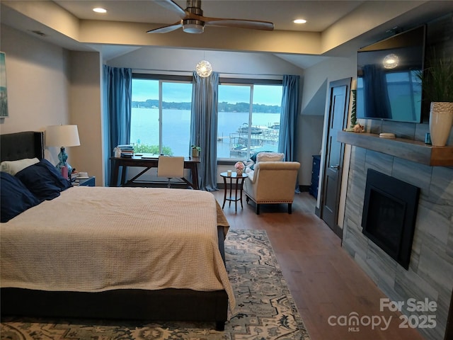 bedroom featuring hardwood / wood-style flooring, a tile fireplace, and ceiling fan