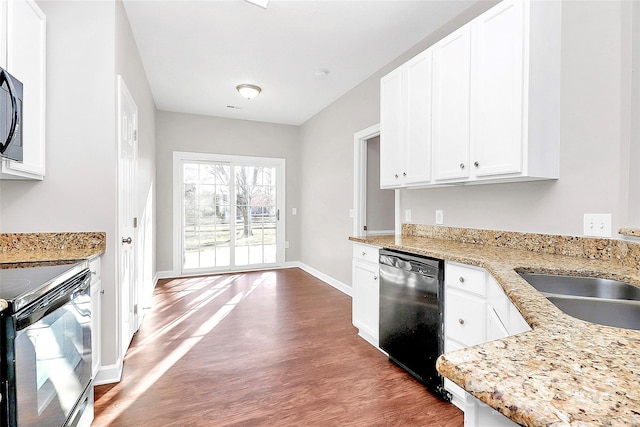 kitchen with wood finished floors, white cabinets, black appliances, light stone countertops, and baseboards