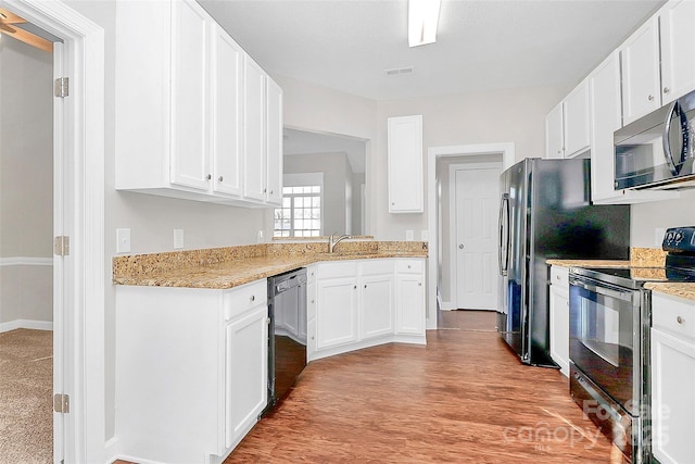 kitchen featuring light wood finished floors, visible vents, black appliances, white cabinetry, and a sink