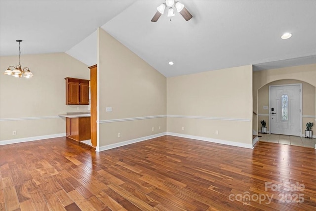 unfurnished living room with ceiling fan with notable chandelier, light wood-type flooring, and vaulted ceiling