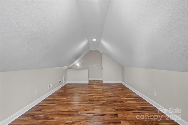 bonus room with lofted ceiling, wood-type flooring, and a textured ceiling