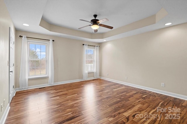 unfurnished room with a raised ceiling, plenty of natural light, and wood-type flooring