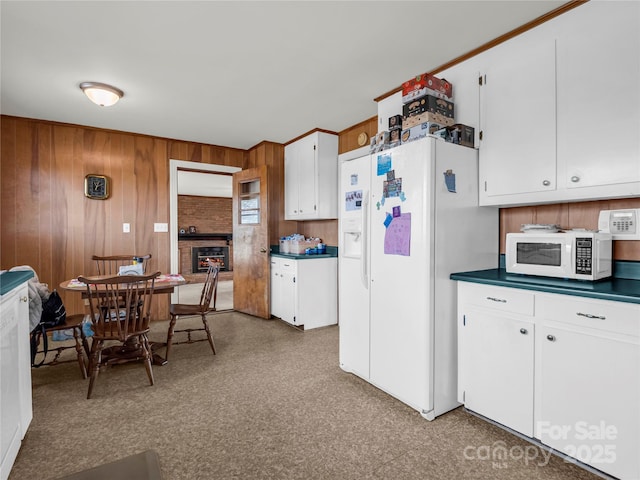 kitchen featuring a brick fireplace, white cabinets, white appliances, and wood walls