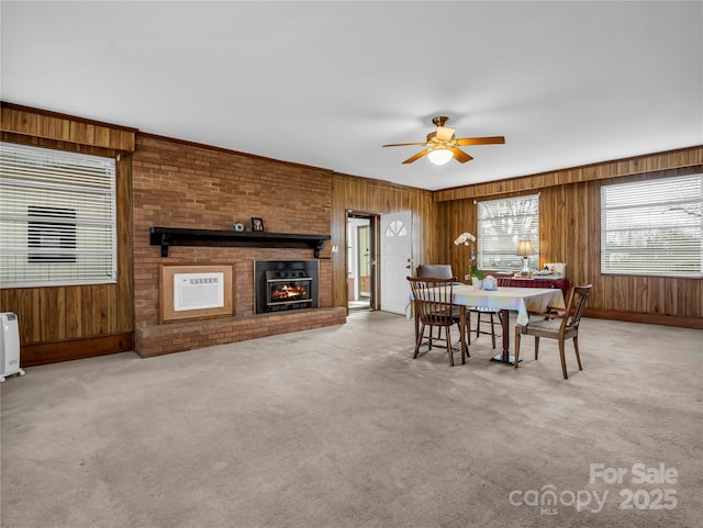 dining area with a brick fireplace, wood walls, ceiling fan, and carpet flooring